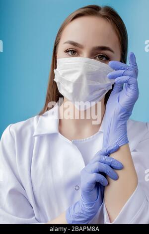 Krankenschwester lächelt hinter der Maske des Chirurgen. Nahaufnahme des Modells der jungen kaukasischen Frau auf blauem Hintergrund. Frau, die Masse trägt, um die Kovid 19 zu schützen Stockfoto