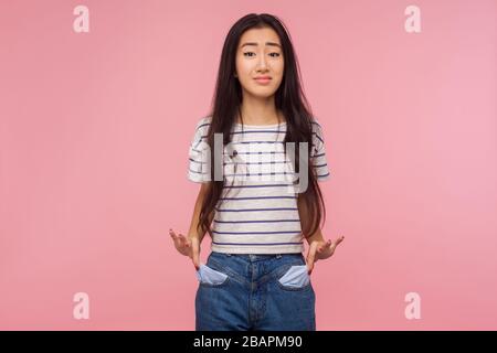 Arbeitslosigkeit und Konkurs. Ärgerliches Mädchen mit brünettem Haar im gestreiften T-Shirt, das aus leeren Taschen herauskommt, sich Sorgen um Schulden macht, kein Geld für das Leben. Stockfoto