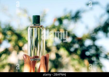 Die Hand der Frau, die eine Flasche Alkohol Gel Desinfektionsmittel zur Reinigung der Hände hält, um Coronavirus Kovid 19 auf den verschwommenen Bäumen im Hintergrund zu verhindern. Stockfoto