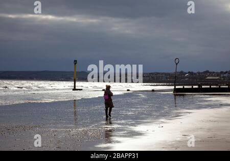 Portobello, Edinburgh, Schottland, Großbritannien. März 2020. Diese einsame Frau geht am Strand entlang am Firth of Forth an diesem bewölkten Morgen bei 3 Grad Celsius mit dem gelegentlichen Sonnenstrahl, der durch die Wolken guckt. Stockfoto