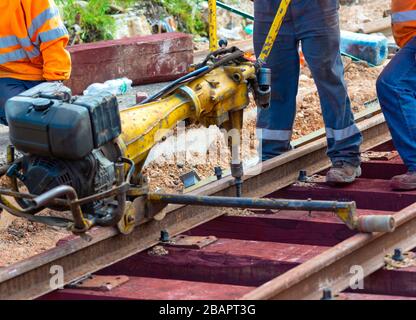 Bahnarbeiter, die die Gleisschiene verschrauben. Detailarbeiter mit mechanischem Schraubenschlüssel Stockfoto