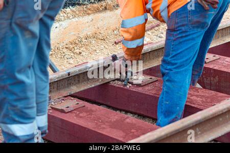 Bahnarbeiter, die die Gleisschiene verschrauben. Detailarbeiter mit mechanischem Schraubenschlüssel Stockfoto