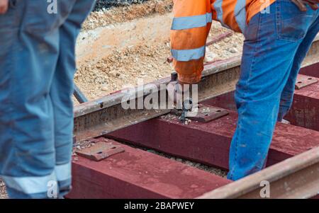 Bahnarbeiter, die die Gleisschiene verschrauben. Detailarbeiter mit mechanischem Schraubenschlüssel Stockfoto