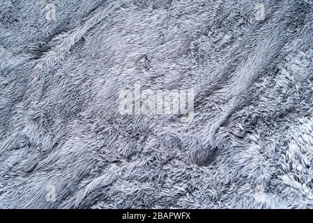 Grauer Hintergrund mit Wolldecke aus Schaffell. Nahaufnahme mit strukturiertem Hintergrund aus schäbigen Fellen. Stockfoto