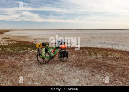 Touristenfahrrad mit Taschen steht am Ufer eines trockenen Salzlakens in der Steppe Kasachstans Stockfoto