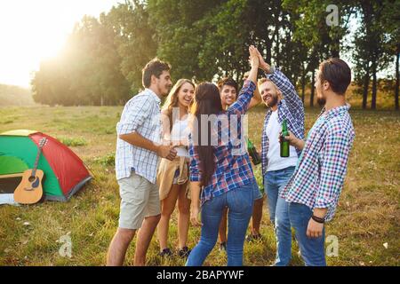 Junge Leute lächeln fröhlich, während sie beim Picknick auf dem Gras stehen Stockfoto