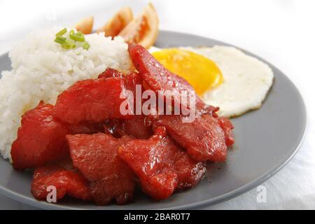 Foto von frisch gekochtem Tocino oder gehärtetem Schweinefleisch, serviert mit gebratenem Reis und Ei mit Gemüse. Stockfoto