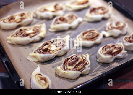 Süße Brötchen mit Zimt auf dem Tablett - Backwaren oder Kochen zu Hause. Ein Detail von rohen Zimtbrötchen - sehr geringe Schärfentiefe. Stockfoto