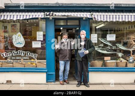 Maskiert gegen das Coronavirus, Greengrocer Leon Abecasis (l) vor seinem Gemüseladen in Presteigne, Powys, Wales, Großbritannien, mit Assistent Paul Clarke Stockfoto