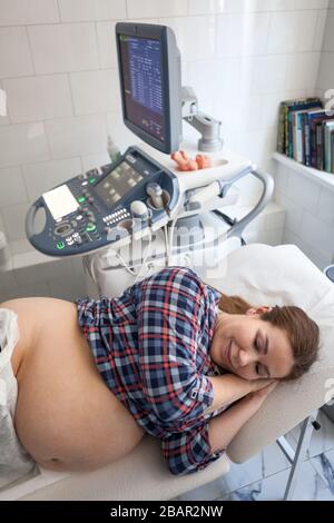 Glückliche schwangere Europäische Frau, bevor sie einen Ultraschall-Scan von einem Geburtshelfer in der Klinik erhalten hat, lag in seitlicher Position Stockfoto