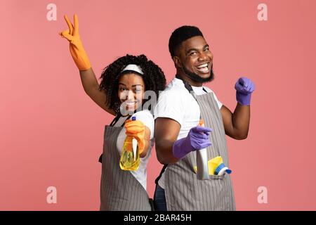 Fröhliches afroamerikanisches Paar mit Spraywaschmitteln, die auf rosa Hintergrund posieren Stockfoto