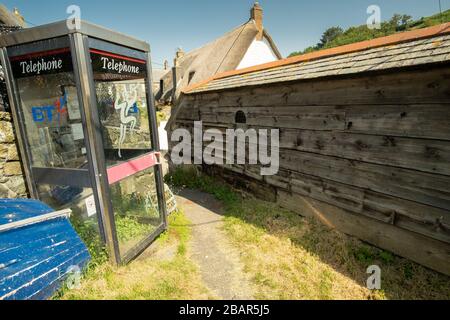 Leerer BT-Telefonkasten neben Path, Boat & Hummertopf mit alter Holzwand im kleinen urigen Fischerdorf Cadgwith, Cornwall, England Stockfoto
