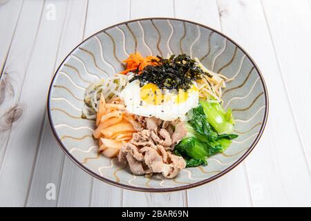 Bibimbap wird als Schüssel mit warmweißem Reis serviert, der mit Gemüse oder Kimchi und Chili Pfefferpaste und Ei und Fleisch in Scheiben gefüllt ist Stockfoto