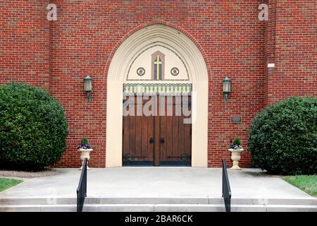 Ein Paar verzierte Kirchentüren aus Eiche vereiteln Ziegelmauern und Hecken Stockfoto