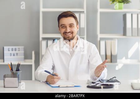 Lächelnde Ärztin gibt an einem Tisch in einer Klinik Beratung. Stockfoto