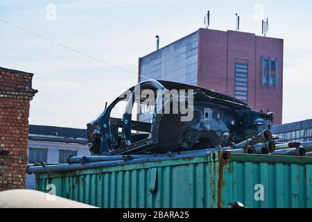 Alter grauer Wagenrahmen zerlegte Wagen mit rostigen Teilen auf der Straße in der Nähe des Zauns. Stockfoto