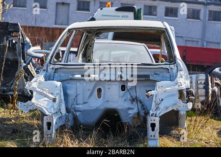 Alter grauer Wagenrahmen zerlegte Wagen mit rostigen Teilen auf der Straße in der Nähe des Zauns. Stockfoto