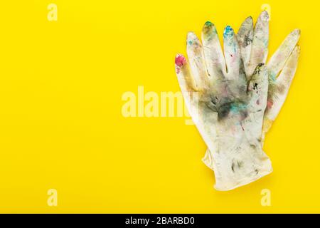 Weiße Gummihandschuhe in Farbflecken auf gelbem Hintergrund. Platz für Text. Das Konzept der Kreativität, der Schöpfung. Stockfoto