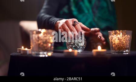 Nahaufnahme der fortunetelleren weiblichen Divination auf Zauberkugel am Tisch mit brennenden Kerzen im dunklen Raum Stockfoto