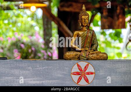 Eine Buddha-Statue aus Bronze in der Lotusposition, die auf einem stilvollen Holzbalken in einem Designer-Interieur steht Stockfoto