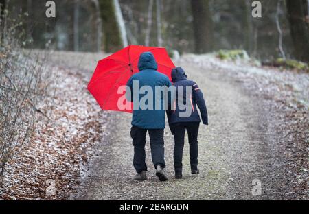 Bielefeld, Deutschland. März 2020. Spaziergänger mit rotem Regenschirm gehen auf einem schneebedeckten Wanderweg im Teutenburger Wald entlang. Nach dem frühlingsartigen Wetter der vergangenen Tage mit zweistelligen Temperaturen schneit es in Teilen von Nordrhein-Westfalen. Credit: Friso Gentsch / dpa / Alamy Live News Stockfoto