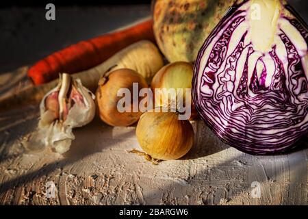 Zwiebeln, Rotkohl und anderes Gemüse auf einem rustikalen Tisch. Natürliches Sonnenlicht und Gemüse. Zutaten für die Suppe. Vegane Ernährung. Stockfoto