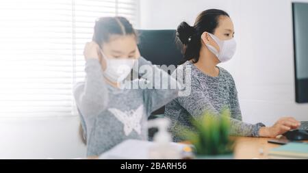 Mutter, die zu Hause mit einer Schutzmaske arbeitet, während sie einen Bericht schreibt. Frau, die von zu Hause aus arbeitet, während sie isoliert ist Stockfoto