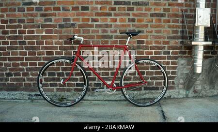 Retro-gestyltes, rotes, singlespeed, festes Zahnrad, isoliert an einer Ziegelwand Stockfoto