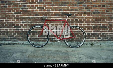 Retro-gestyltes, rotes, singlespeed, festes Zahnrad, isoliert an einer Ziegelwand Stockfoto
