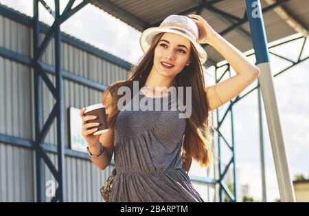 Sie reist gern. Porträt der schönen und jungen Frau in Kleid und Hut Tasse Kaffee in der Hand halten und Hut einstellen, während sie im Zug steht Stockfoto