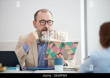 Portrait des leitenden bärtigen Professors, der mit der Klasse spricht, während er am Schreibtisch in der Schule sitzt, Kopierraum Stockfoto