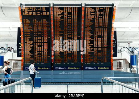 Passagiere vor einem großen Flugplan, der Flugplanflüge auf dem Flughafen Paris Charles de Gaulle anzeigt. Stockfoto