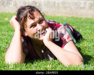 Frau mittleren Alters, die bei Sonnenschein auf dem Gras liegt, Großbritannien Stockfoto