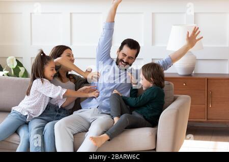 Überfreudige junge Frau mit verspielten kleinen Kindern, die lachenden Ehemann kitzeln. Stockfoto