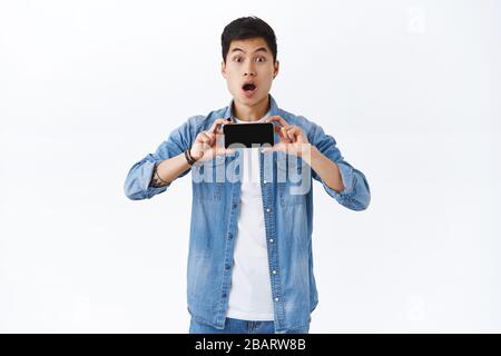 Technologie, Online Lifestyle Konzept. Porträt von staunenden jungen beeindruckt asiatischen Mann zeigt neue Trailer des Films auf dem Smartphone-Bildschirm, halten mobile Stockfoto