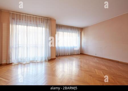 Leeres großes Zimmer mit Holzboden und weißen Vorhängen im Inneren der Wohnung Stockfoto