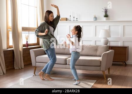 Überglücklich tanzte junge Mama Babysitter mit Mädchen zur Musik. Stockfoto