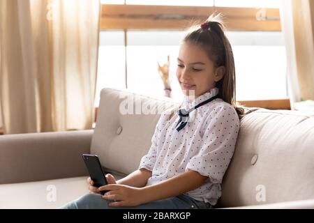 Ziemlich glückliches kleines Schulmädchen, das Online-Spiel auf dem Handy spielt. Stockfoto