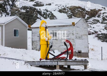 Schnitzen eines Fischers in einem gelben Regenslicker mit Ankern in Fogo, auf Fogo Island, Neufundland, Kanada [keine Eigentumsfreigabe; für editori verfügbar Stockfoto