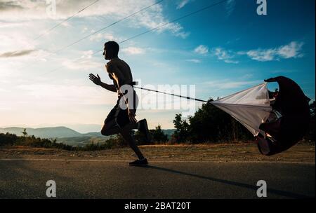 Athlet Jogger, der Kardio mit Sportfallschirm ausarbeitet, der auf Querfeldeinrennen bergauf im Freien aufgeht Stockfoto