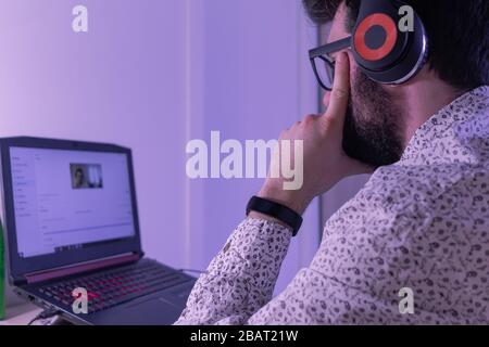 Der junge Geschäftsleute nimmt mit seinen Kollegen an einem Anruf Teil. Er verwendet die Kopfhörer, um den Anruf in besserer Qualität zu hören Stockfoto