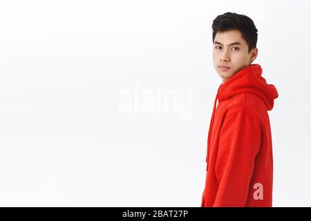 Porträt von schönen asiatischen Hipster Kerl in roten Hoodie im Profil stehen und drehen Gesicht zur Kamera mit bestimmten, ernst aussehenden Ausdruck Stockfoto