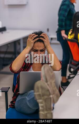 Eine nervöse Büroangestellte mit ihren Beinen auf ihrem Schreibtisch und ihrem Laptop in ihrem Schoß, die einen harten Tag hatten. Stockfoto