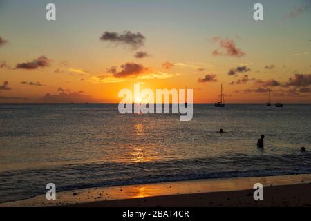 Wunderschöner oranger und gelber Sonnenuntergang, die Horizont-Linie und der Himmel wenige Wolken, die Reflexion der Sonne an Meer und Ufer, Menschen im Meer mit Jachten und Booten Stockfoto