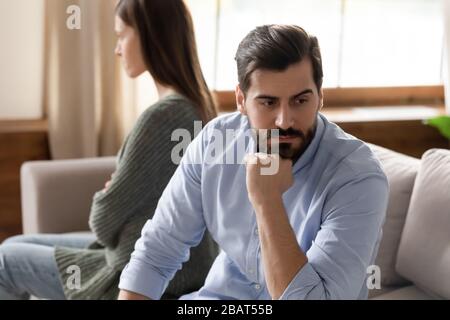 Konzentrieren Sie sich auf gestressten jungen Mann, der getrennt von beleidigter Frau sitzt. Stockfoto