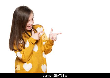 Schönes junges Mädchen im senfgelben Pullover, das sich beim zeigen auf die Seite verhüllt. Studio mit Taille oben, aufgenommen auf weißem Hintergrund. Stockfoto