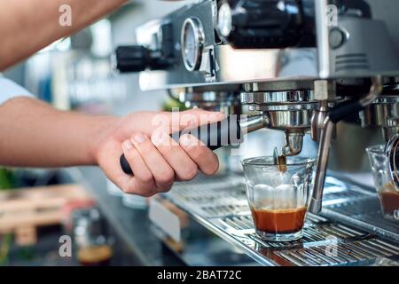 Kaffeelaffee. Junger Barista im Café, der Espresso-Shot-Schüsse aus der Nähe mit einer Maschine gießt Stockfoto