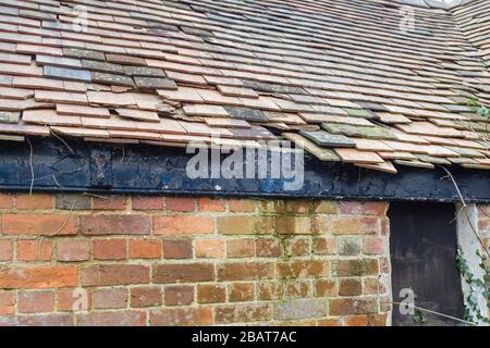 Beschädigte Dachziegel aus Ton auf einem Satteldach auf einem derben Haus in England, Großbritannien Stockfoto