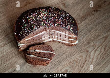 Köstlicher Schokoladenkuchen auf dem Tisch auf dunklem Hintergrund. Auf einem Holzständer mit einem Stück geschnittenem Kuchen. Draufsicht. Kopierbereich. Stockfoto