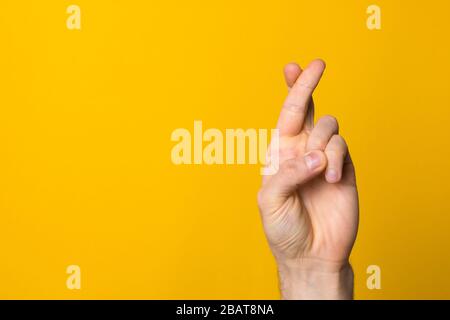 Finger kreuzten das Zeichen der Hoffnung. Nahe die Hand des Menschen, die den Glauben vor gelbem Hintergrund symbolisiert Stockfoto